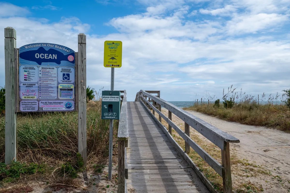 The image presents a beach access sign and a wooden walkway leading toward the sandy shore, with the ocean in view. The scene feels relaxed and welcoming, inviting families to embark on their next seaside adventure.