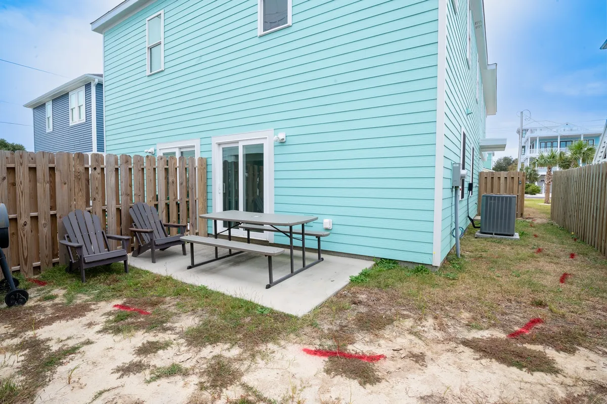 A fenced patio and yard area with turquoise exterior walls, wooden picnic table, and Adirondack chairs—inviting spaces for outdoor dining, relaxing, and group gatherings, all safely enclosed for pets and children.