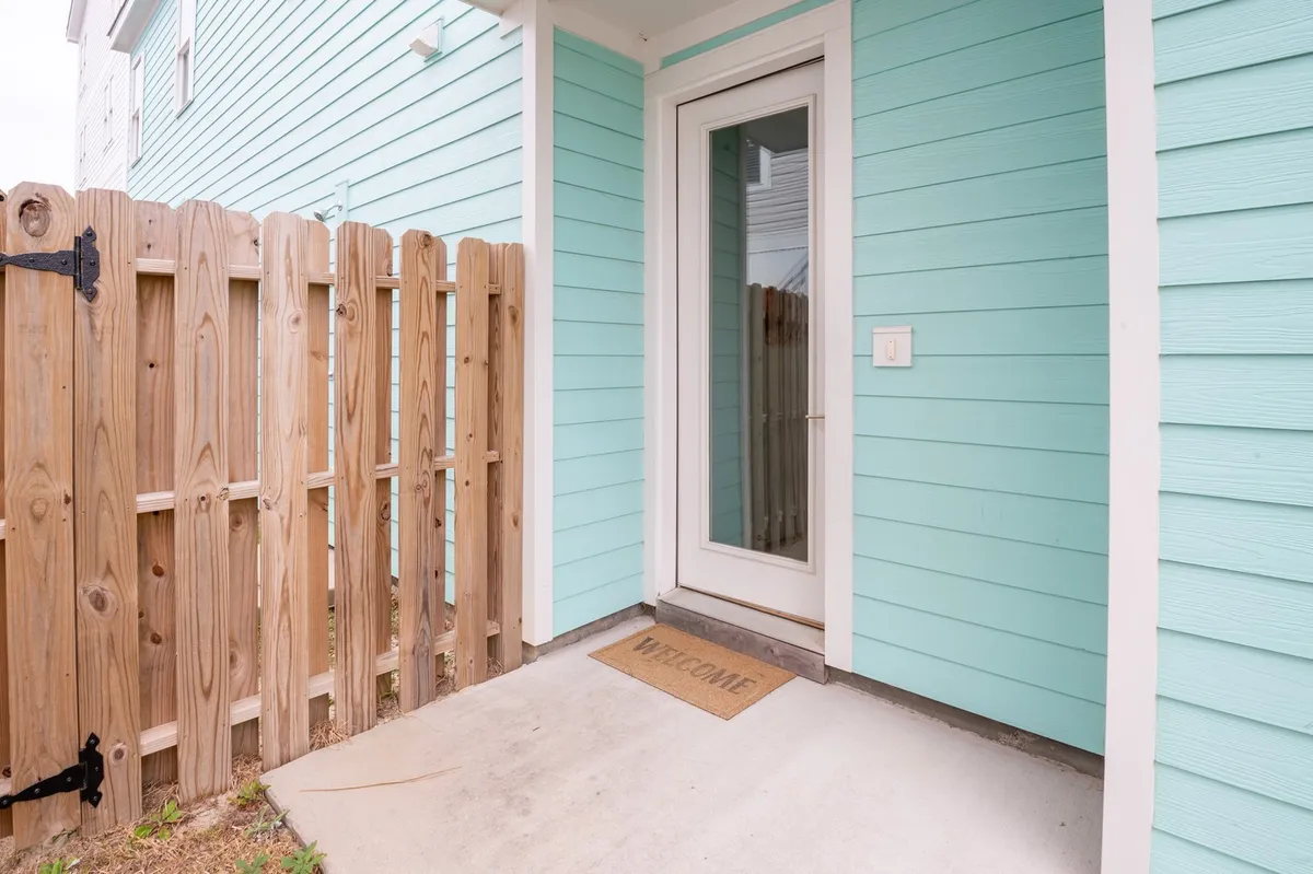 A warm, welcoming exterior view of the vacation home's front door, turquoise wall, and wooden fence. The scene conveys the first impression as guests and their pets arrive, highlighting the fenced outdoor space.