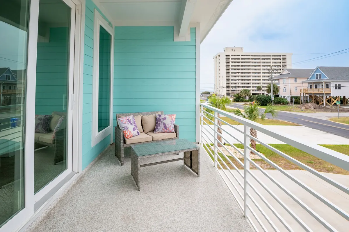 This image features an outdoor patio area with comfortable furniture set against turquoise walls, offering a partial view of surrounding buildings. The setting suggests a relaxed space perfect for enjoying morning coffee or gathering for sunset cocktails, with a sense of openness that connects the home to the local neighborhood vibe.