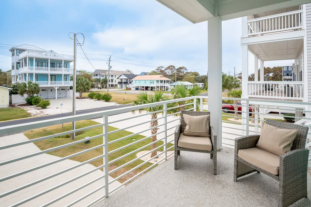 A serene balcony scene featuring comfortable seating overlooking the street, with views of neighboring homes and palm trees. The image captures the essence of island life, showing a tranquil spot ideal for watching the neighborhood activity or enjoying a breeze.