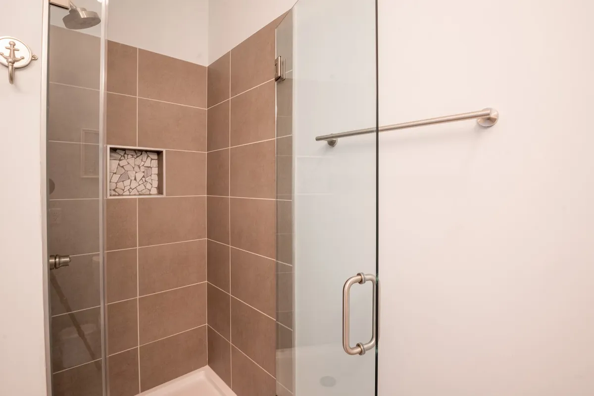A sleek, modern shower area with a glass door, stone inlay, and a convenient towel bar. The space feels spa-inspired and serene—ideal for refreshing after a day at the beach.