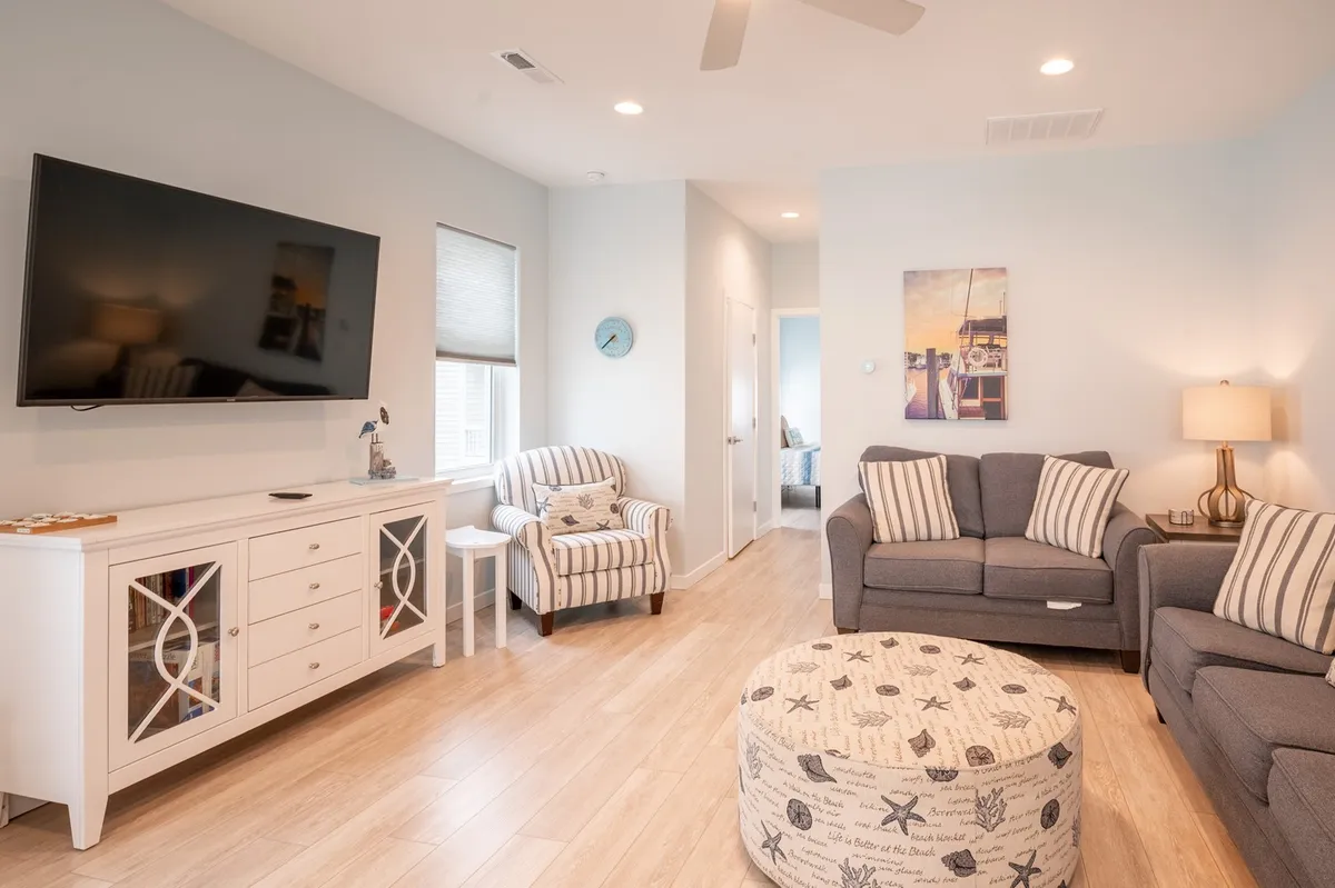 The living area is showcased with a cozy sofa, striped armchair, decorative ottoman, and a TV—suggesting a comfortable spot for streaming shows or playing games. The arrangement invites relaxation and socializing, reinforcing the room's role as a gathering place.