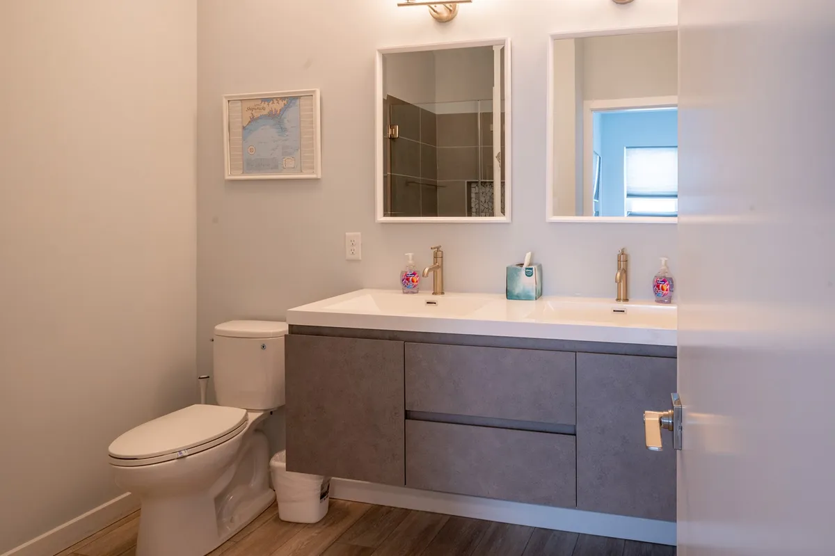 A spacious, modern bathroom with a double floating vanity, two framed mirrors, stylish lighting, and subtle wall art. The space is bright, inviting, and signals luxury and modern comfort.